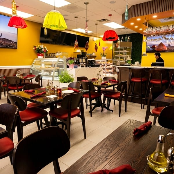 A vibrant restaurant interior with yellow walls, red chairs, dark wood tables, and a bar area.