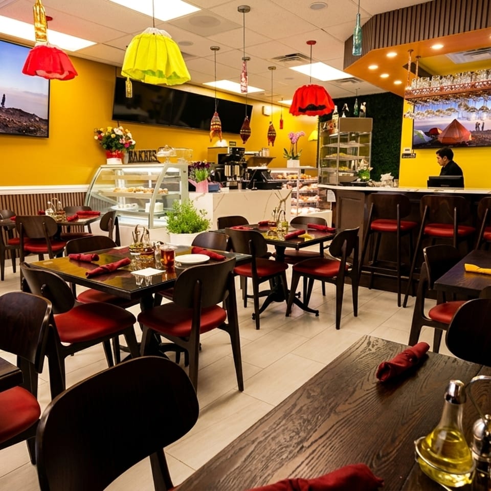 A vibrant restaurant interior with yellow walls, red chairs, dark wood tables, and a bar area.