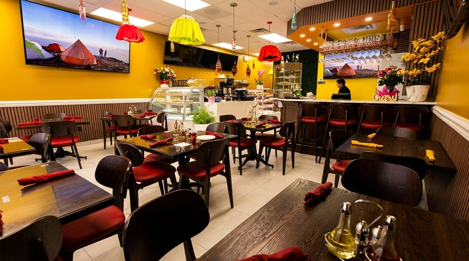 A vibrant restaurant interior with yellow walls, red chairs, dark wood tables, and a bar area.