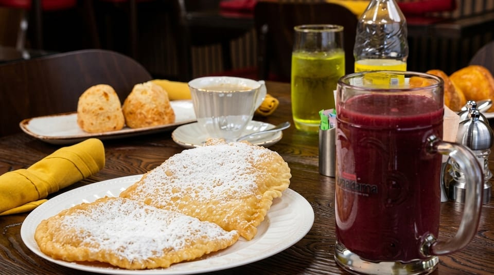 A table laden with a breakfast spread including pastries, coffee, juice, and a berry smoothie.