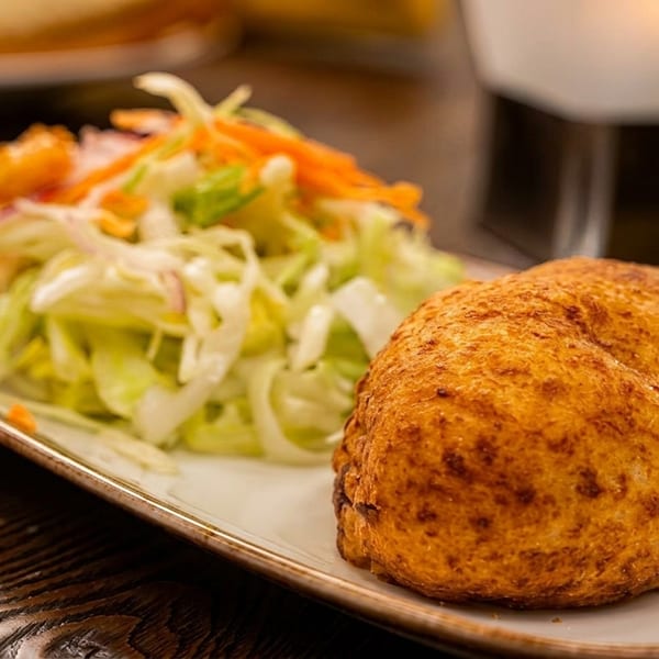 A golden-brown fried pastry and a fresh green salad with shredded carrots on a white plate.